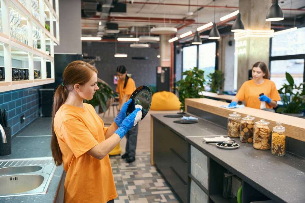 Cleaning female work team cleaning in the kitchen area of the coworking, women in uniform and protective gloves