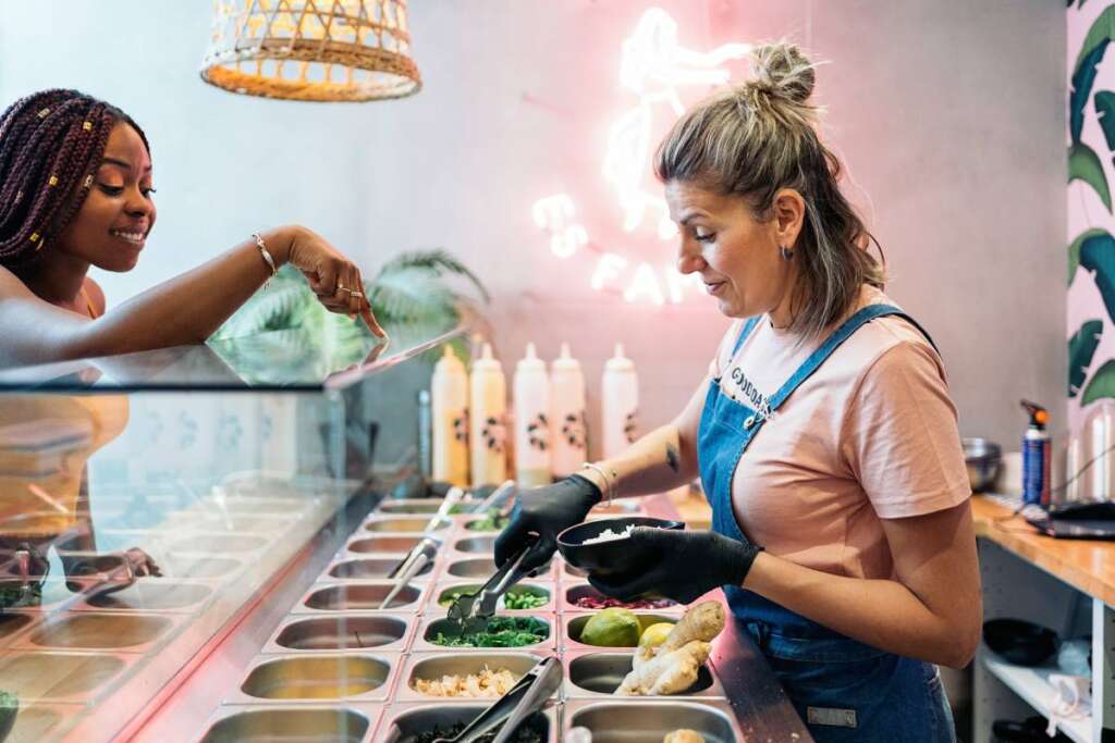 Pretty african woman choosing the ingredients of her poke bowl in a restaurant.