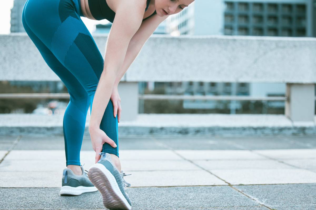 Closeup of one caucasian woman holding her sore ankle while exercising outdoors. Female athlete suf