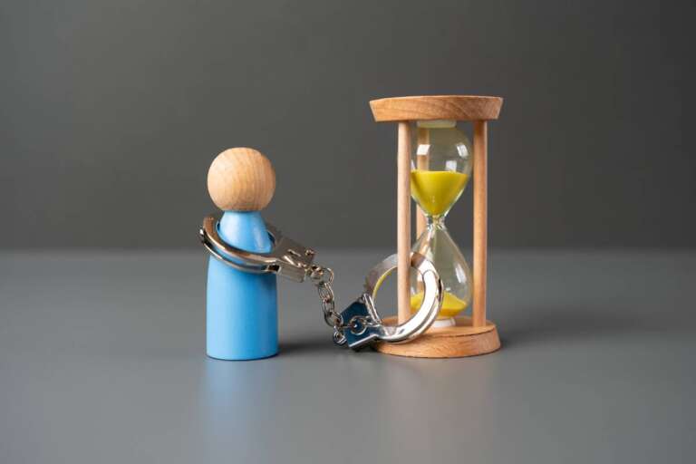 A man is handcuffed to an hourglass. The concept of life time limitation or deprivation. Be patient. Be limited in time.