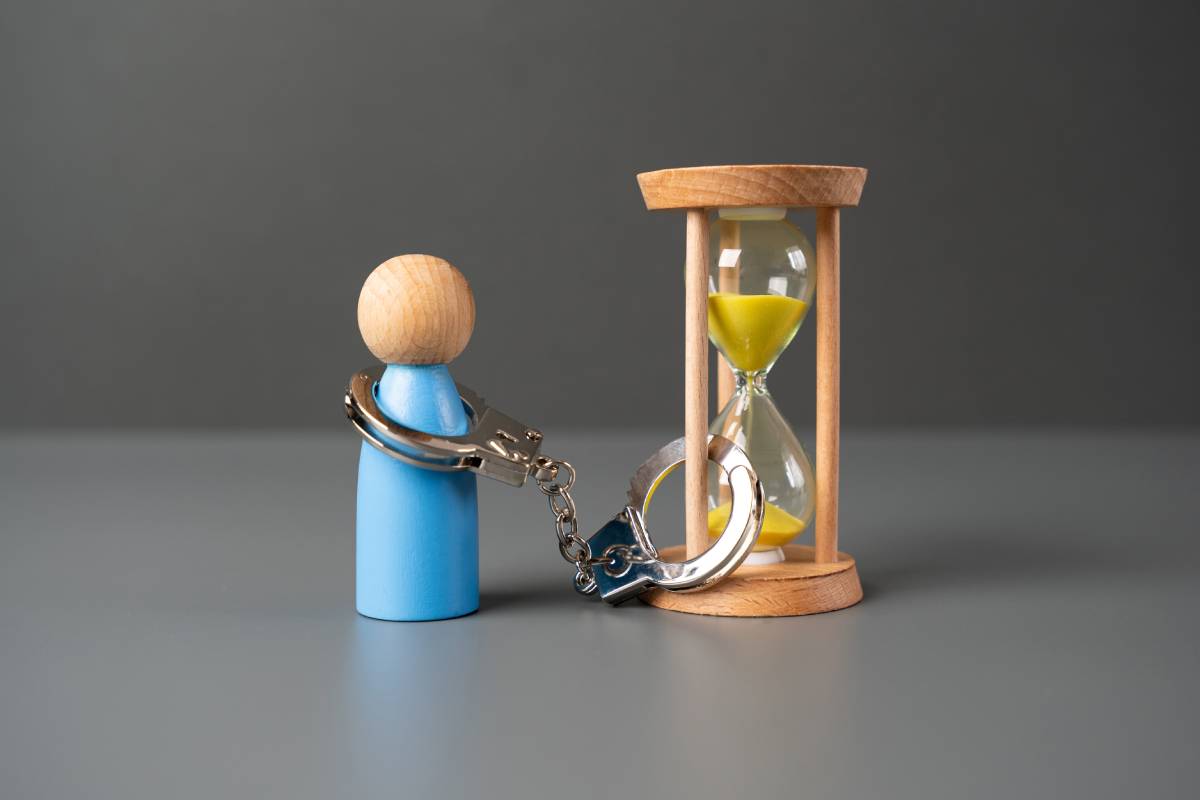 A man is handcuffed to an hourglass. The concept of life time limitation or deprivation. Be patient. Be limited in time.