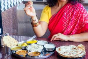 close up photo of Indian traditional vegetarian thali from rice, dal, potatoes, tomato salad on metal plate ,female hands roti india tortilla Chapati