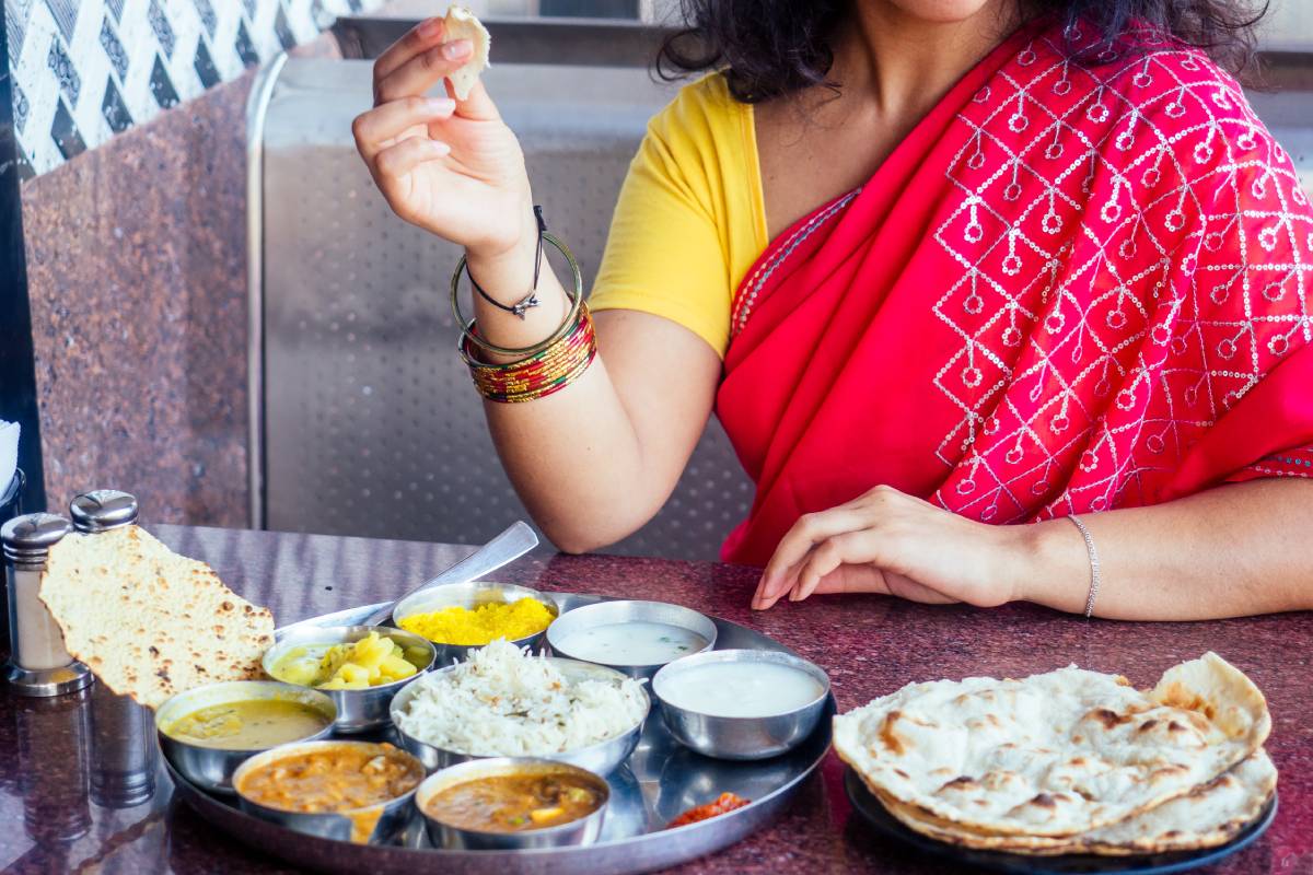 close up photo of Indian traditional vegetarian thali from rice, dal, potatoes, tomato salad on metal plate ,female hands roti india tortilla Chapati
